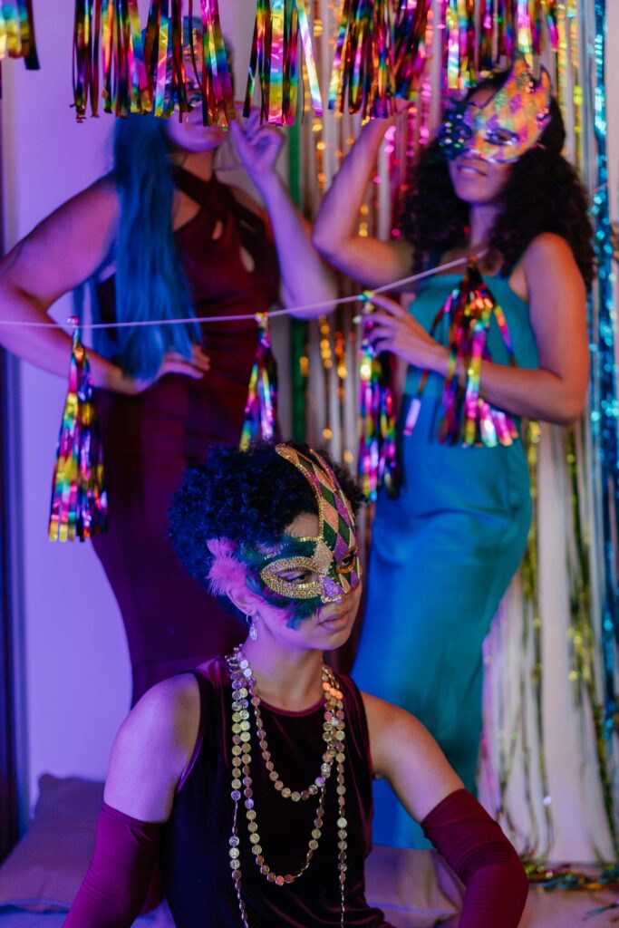 A vibrant indoor masquerade party featuring women in elegant dresses with festive masks and decorations.